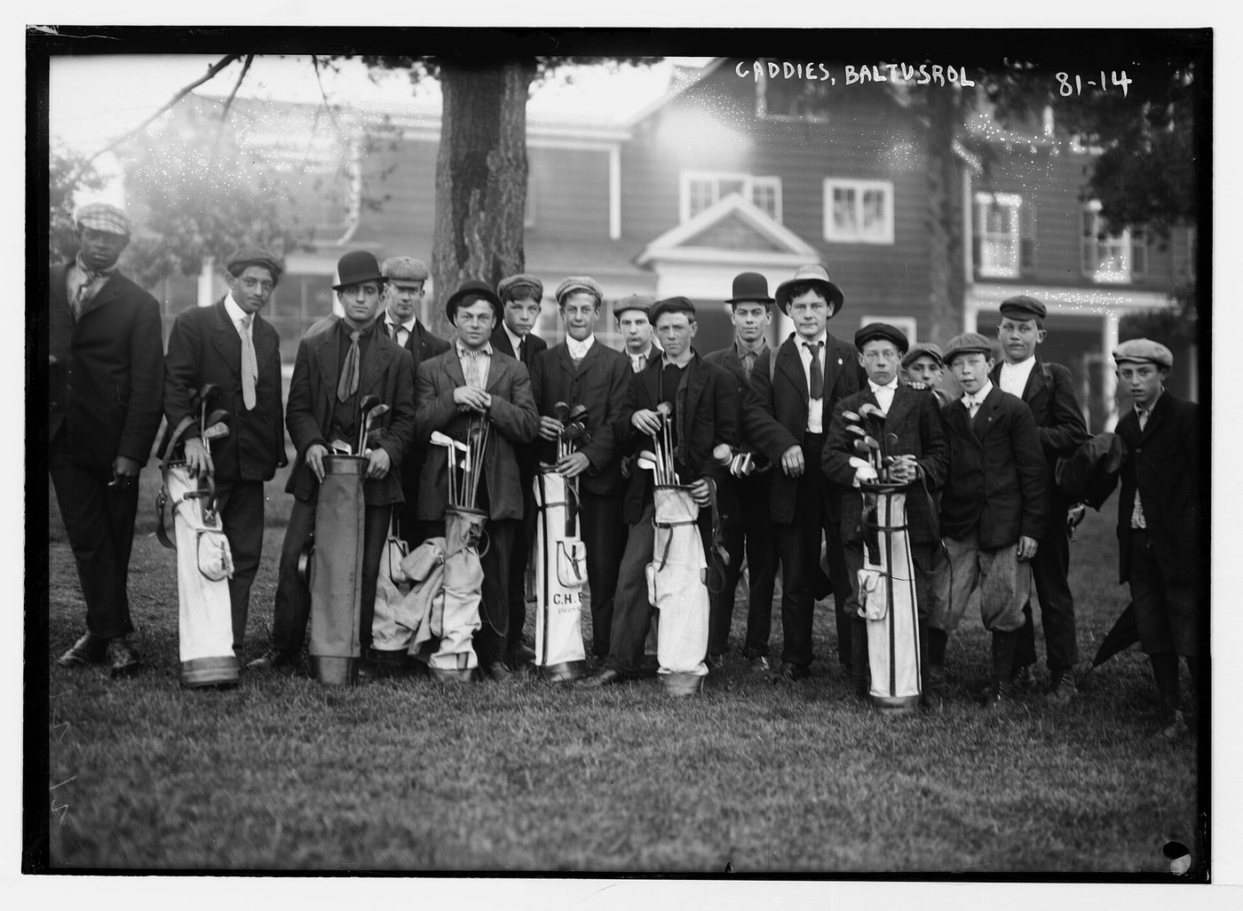 A group of young caddies holding members' golf bags outside the clubhouse at Baltusrol Golf Club in an early 1900s photograph