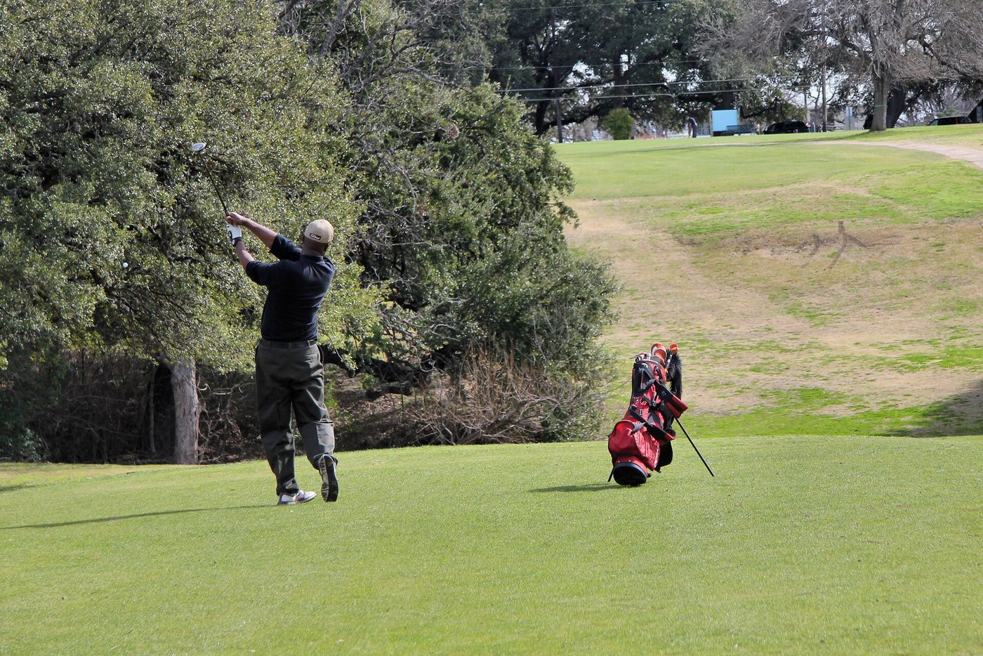 A golfer tees off on the ninth hole at Hancock Golf Course in Austin under live oaks