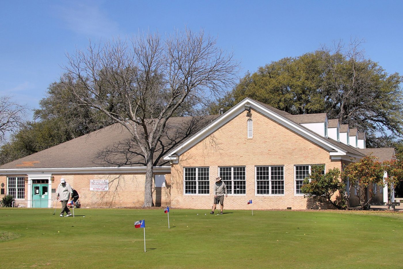 Golfers on the putting green in front of the Lions Municipal Golf Course clubhouse in Austin