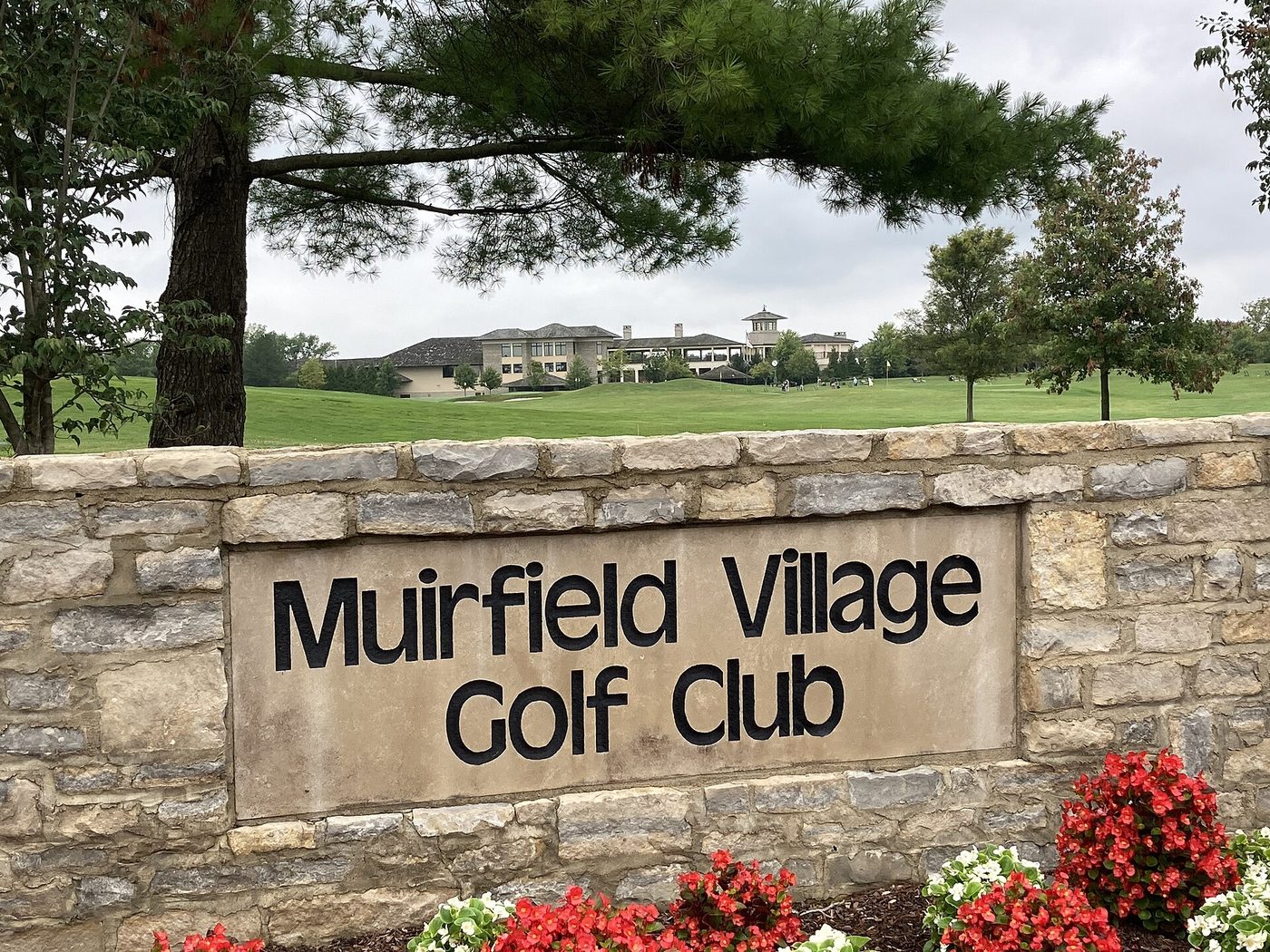 The stone Muirfield Village Golf Club sign with the clubhouse behind in Dublin, Ohio