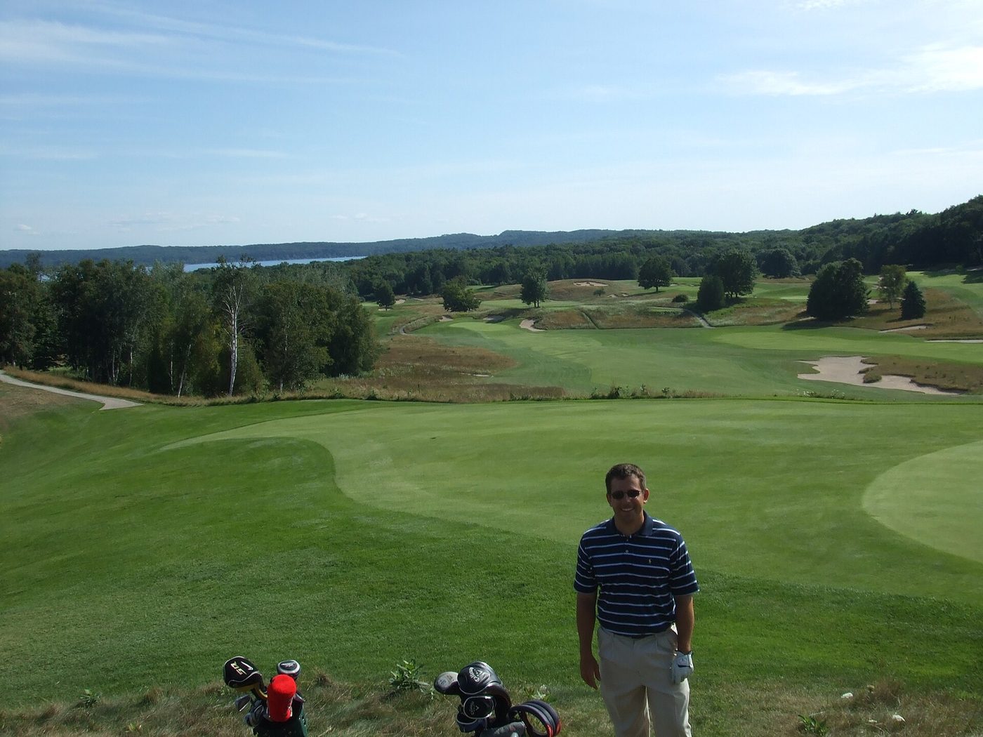 Rolling fairways and bunkers at Crystal Downs seen from the ninth green, with a lake and wooded hills on the horizon