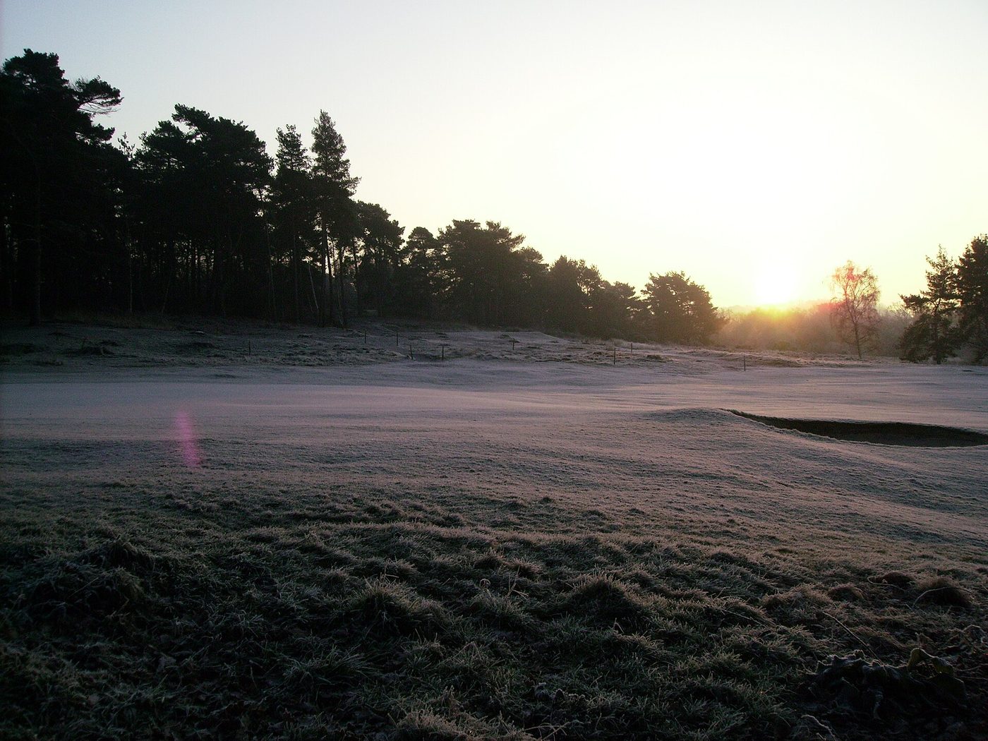 Low winter sun rising over frost-covered turf and heathland at Reigate Heath Golf Club