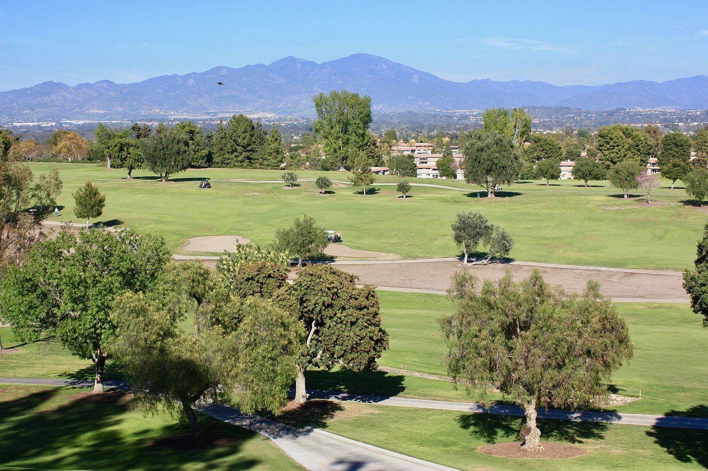 Tree-lined fairways at the Laguna Woods Village golf course seen from the clubhouse, with the Santa Ana Mountains in the distance