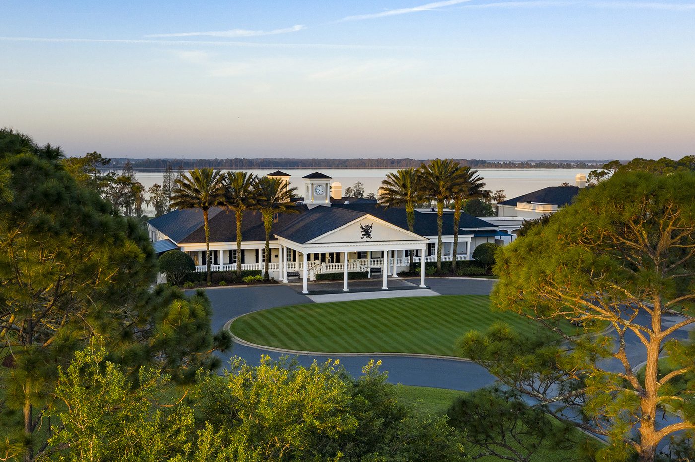 The white colonnaded clubhouse at Lake Nona Golf & Country Club in Orlando, with palms, a round lawn and the lake behind at dawn