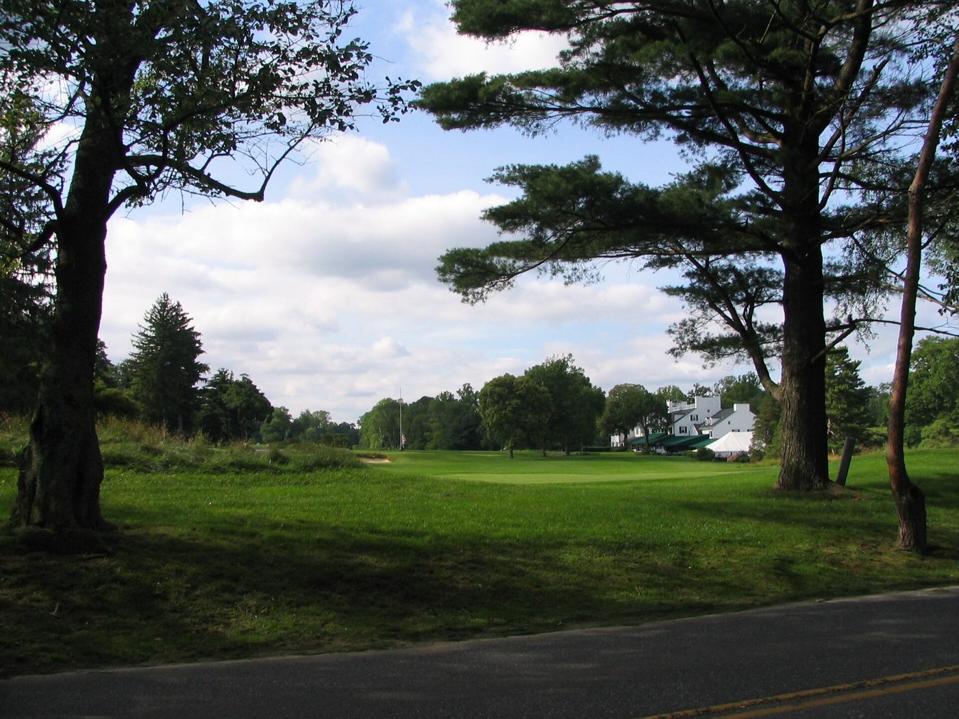 Tall pines framing a green at Merion Golf Club in Ardmore, Pennsylvania, with the clubhouse in the distance