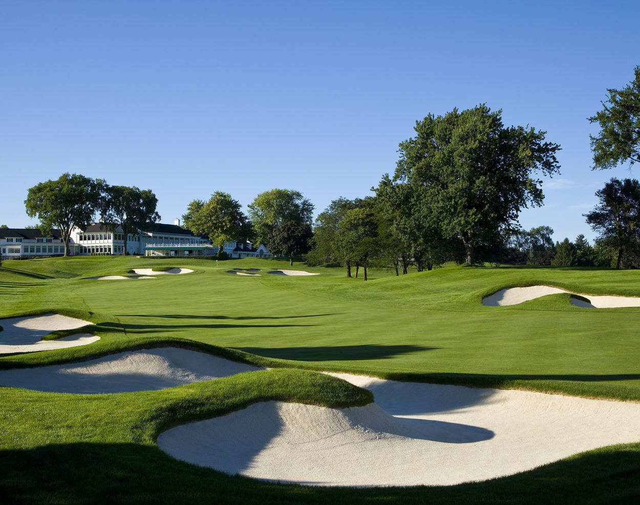 Deep white bunkers in front of a green at Oakland Hills Country Club, with the old clubhouse behind, one of the best golf courses in Michigan