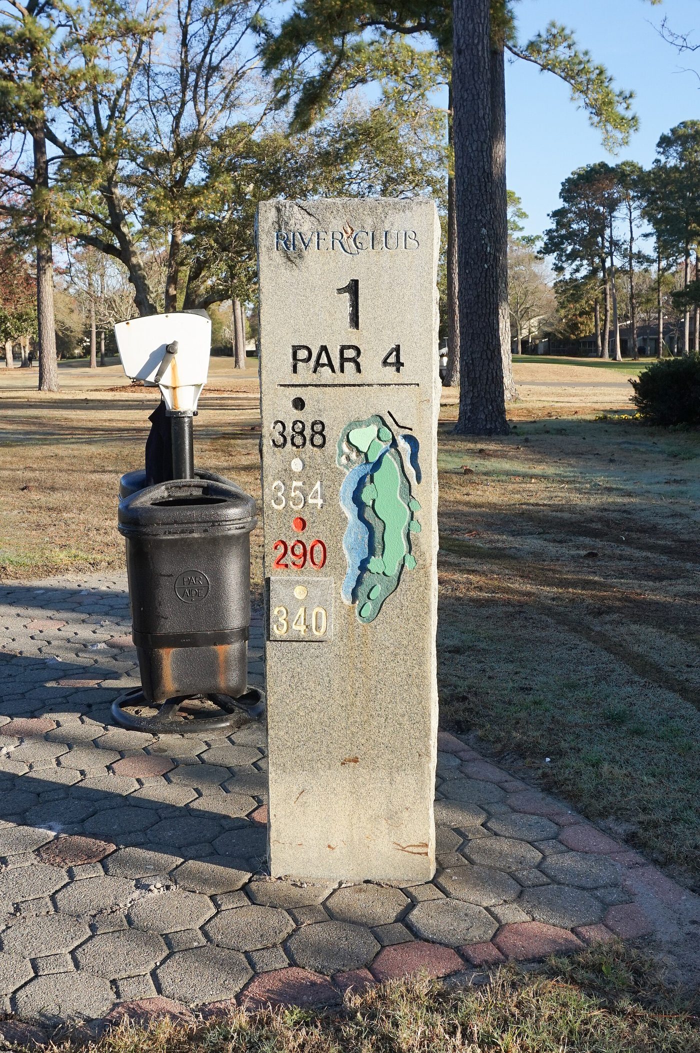 The stone marker for the par-4 1st hole at the River Club on Pawleys Island, with a ball washer beside it and pines behind