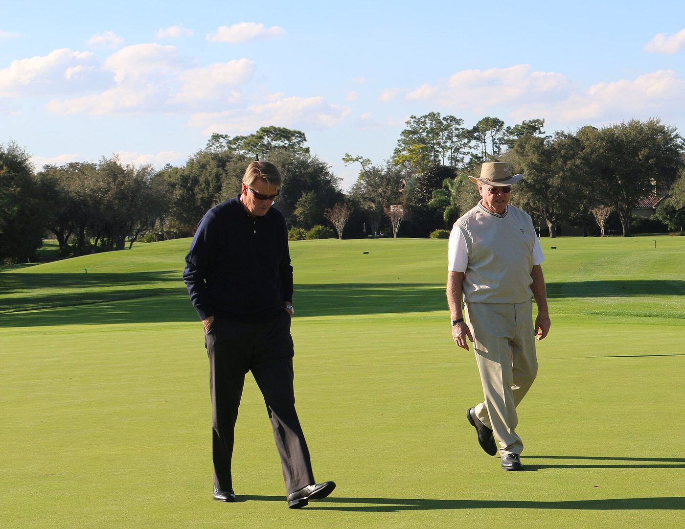 Golf course architect Tom Fazio walking across a green at Lake Nona Golf & Country Club with the club's director of golf