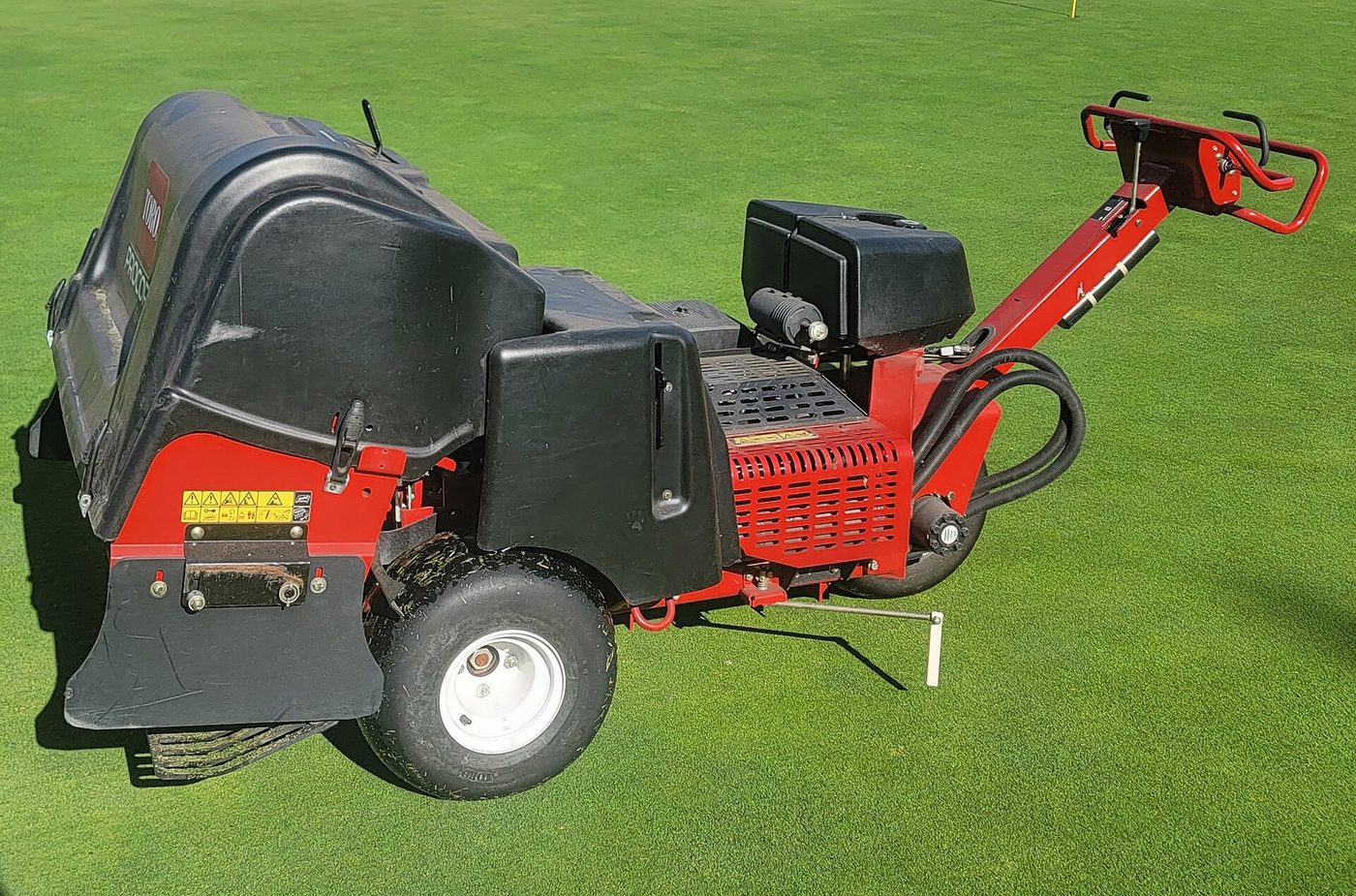 The back of a Toro ProCore 648 core aerator on a green, showing the row of hollow tines beneath the hood