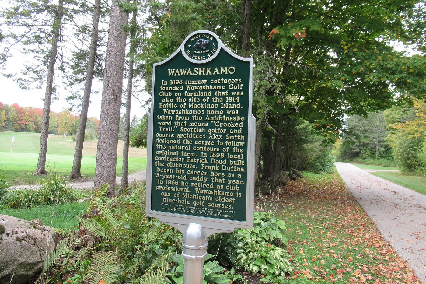 The Michigan historical marker at Wawashkamo Golf Club on Mackinac Island, with a fairway visible through the trees