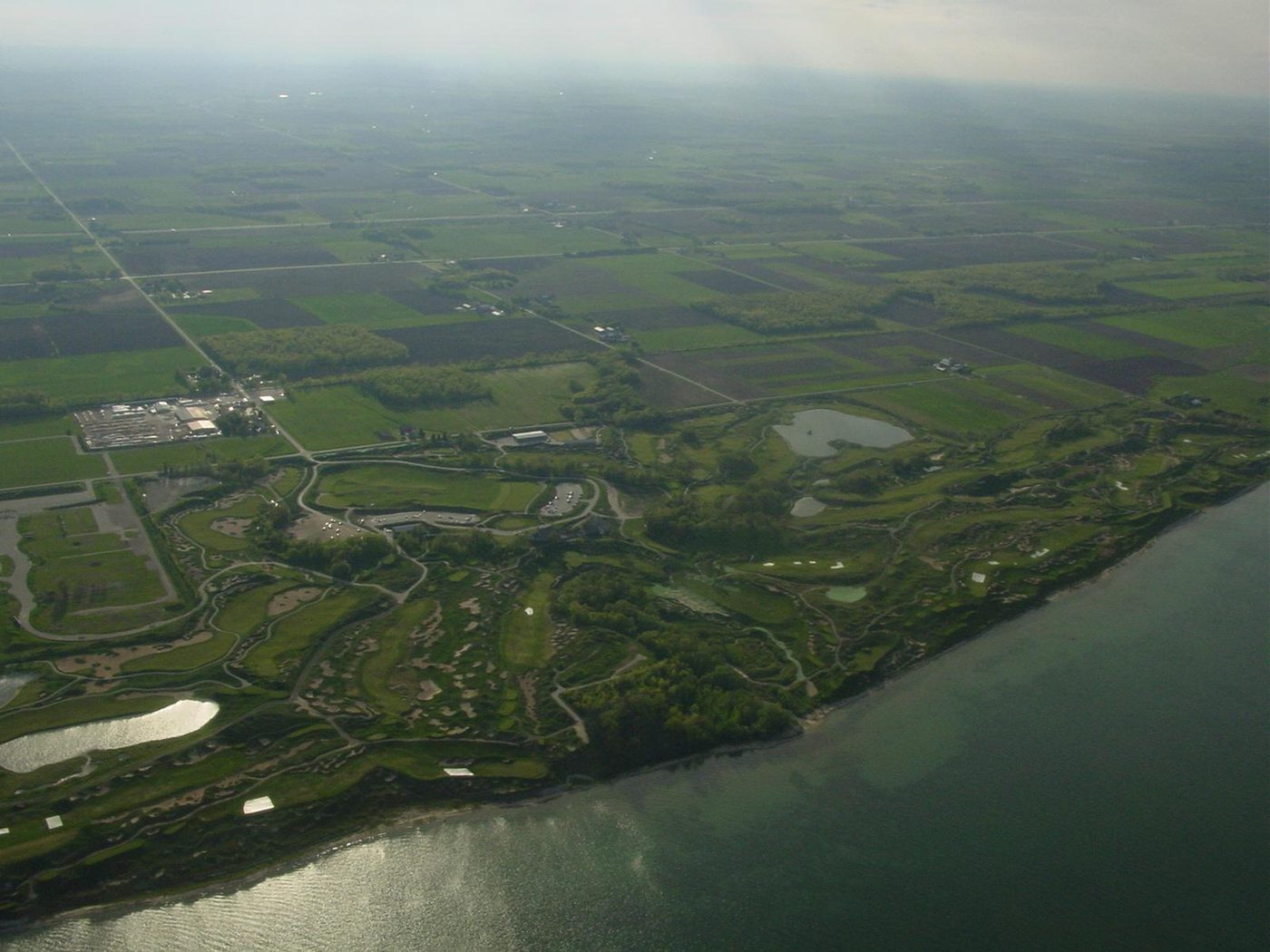 Aerial view of Whistling Straits along the Lake Michigan shore, with farmland stretching inland behind the course