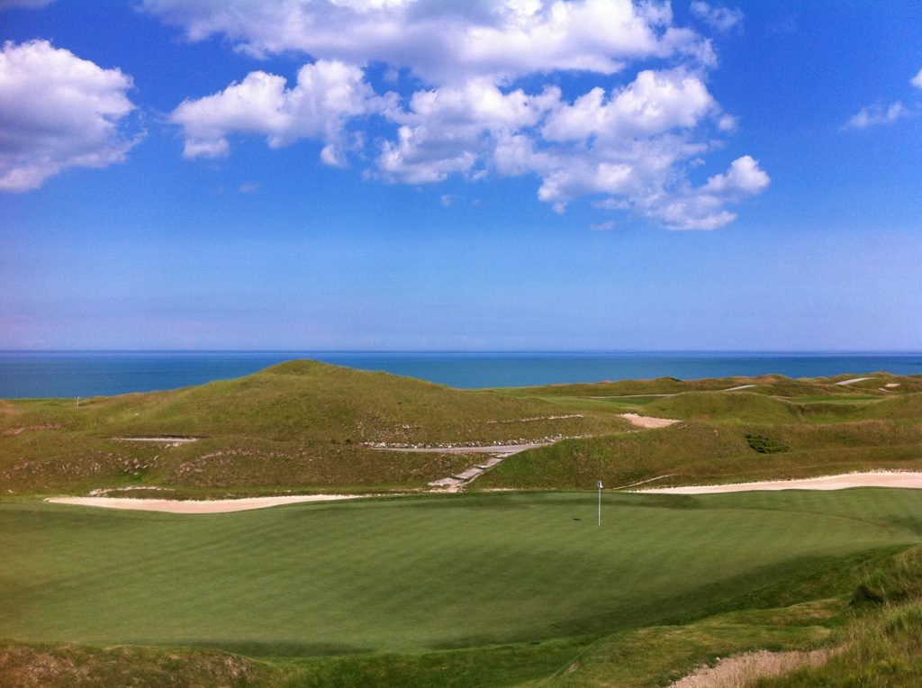 A green on the Irish Course at Whistling Straits surrounded by grassy dunes, with Lake Michigan on the horizon
